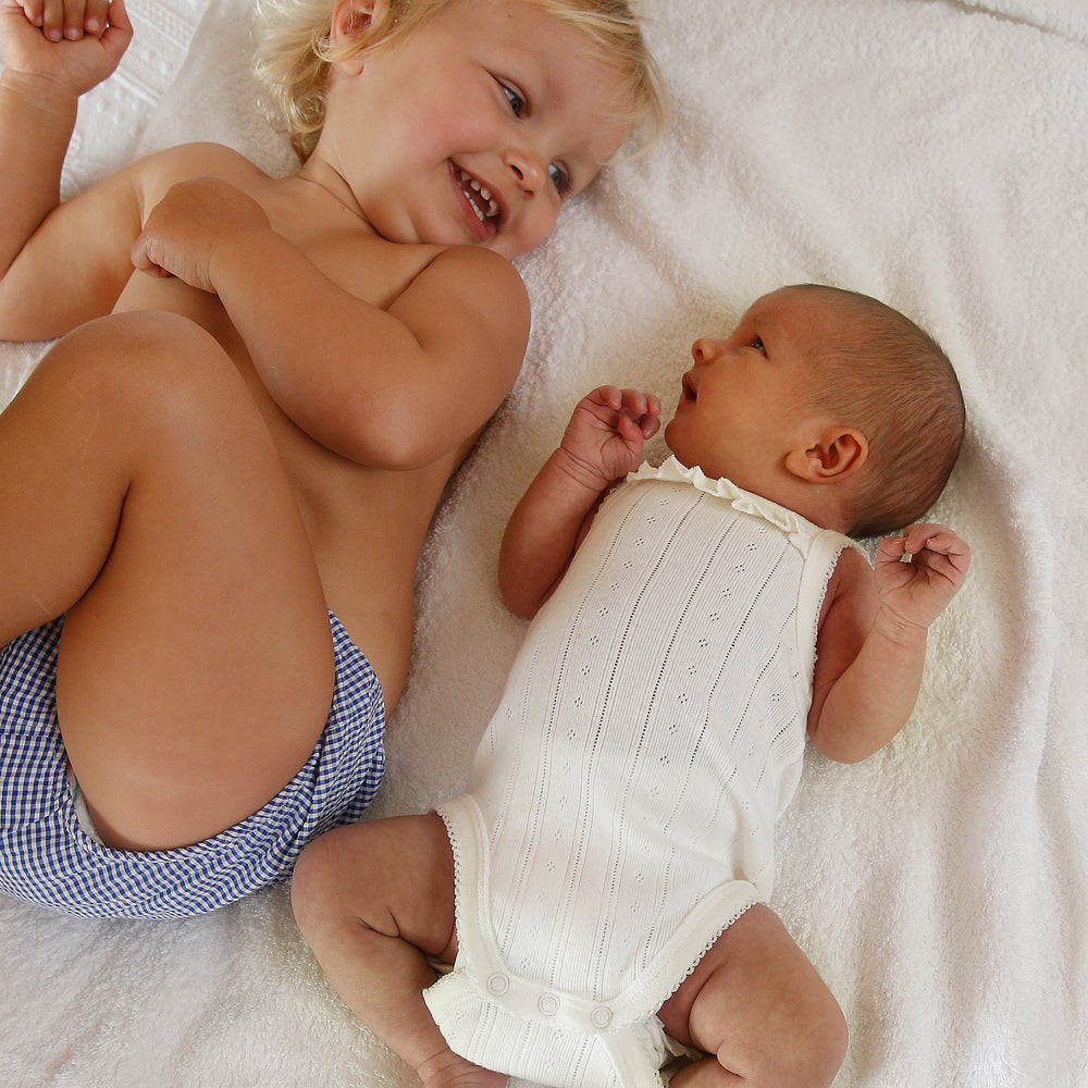 Two children, one older and one younger, lying on a white blanket.