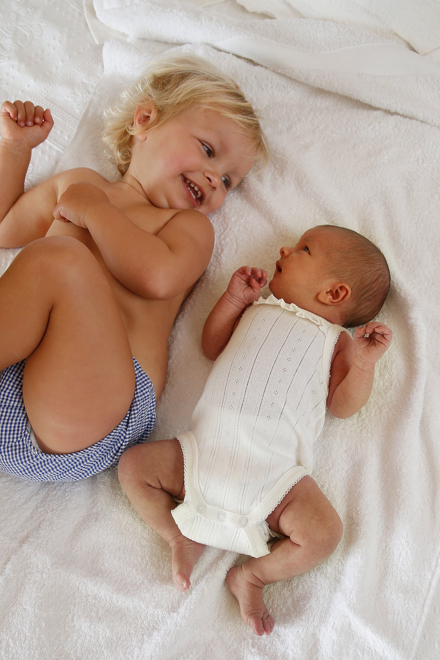 Two children, one older and one younger, lying on a white blanket.